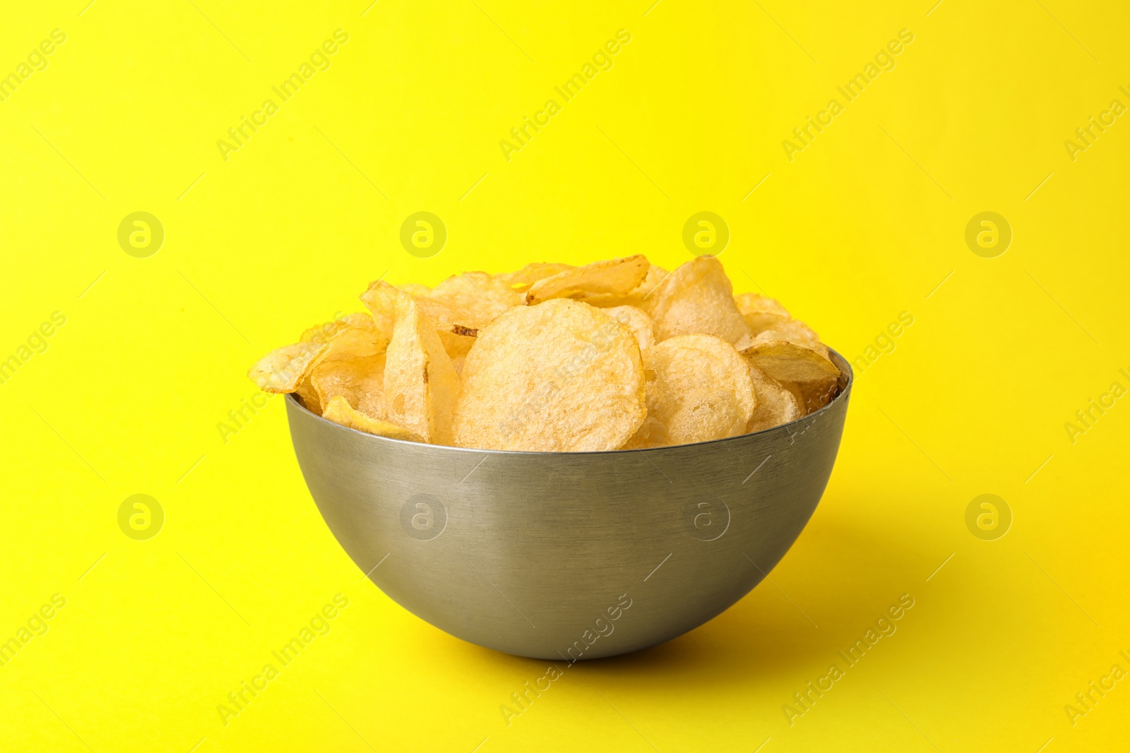 Photo of Delicious crispy potato chips in bowl on color background