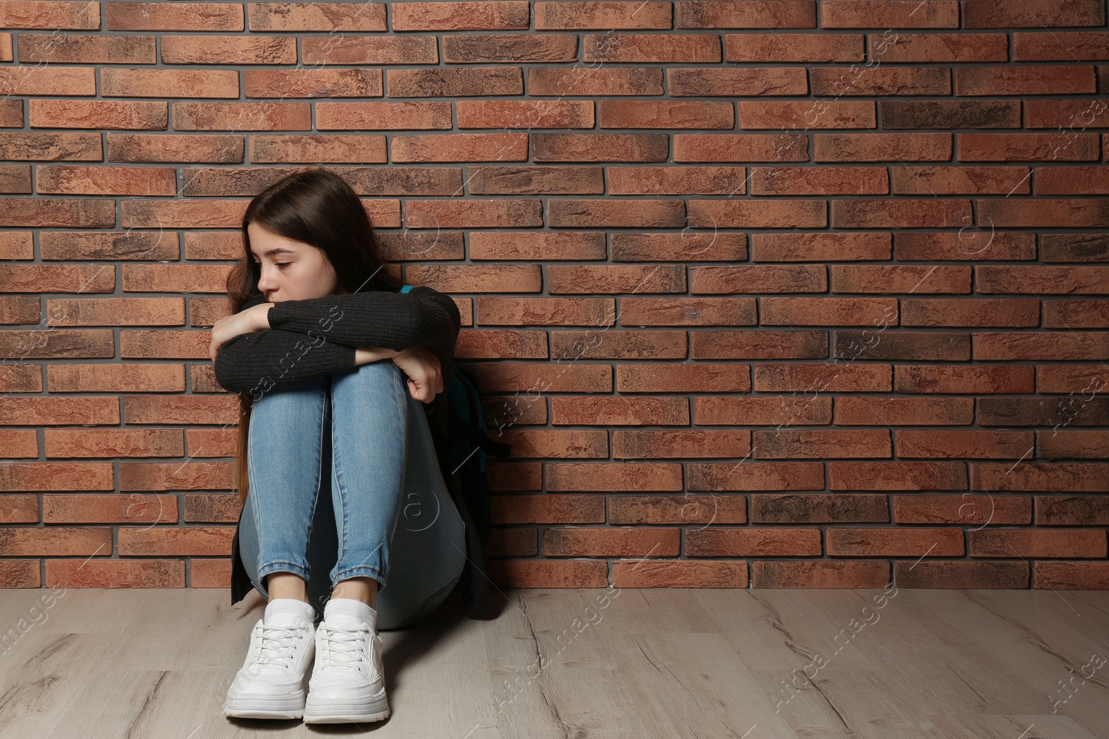 Photo of Upset teenage girl sitting on floor near wall. Space for text