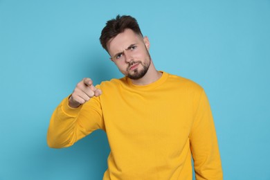 Photo of Aggressive man in yellow sweatshirt pointing at something on light blue background