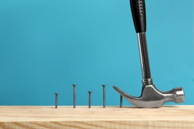 Photo of Hammer pulling metal nail out of wooden surface against light blue background, space for text