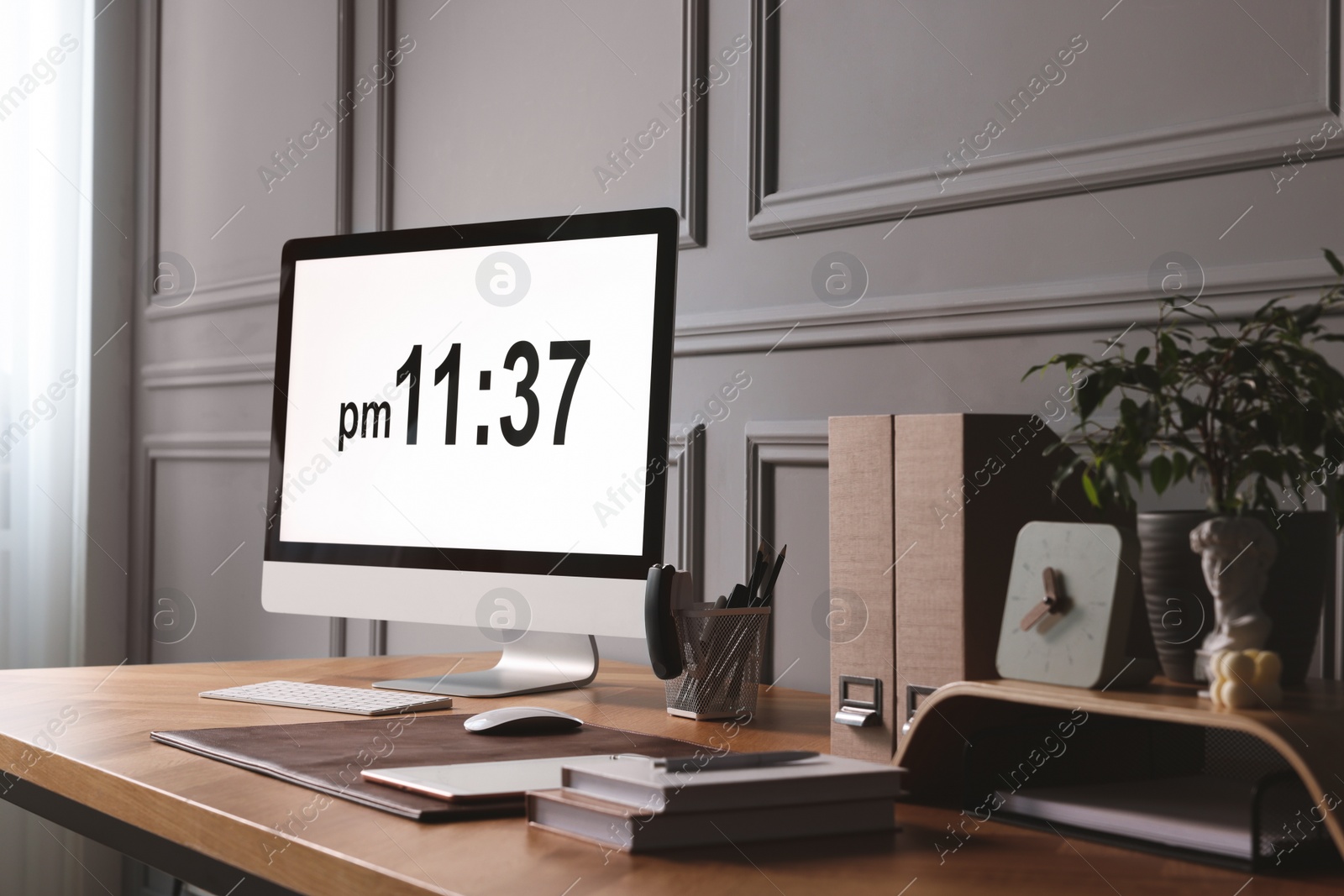 Photo of Stylish workplace with computer, houseplant and stationery on wooden desk near grey wall at home