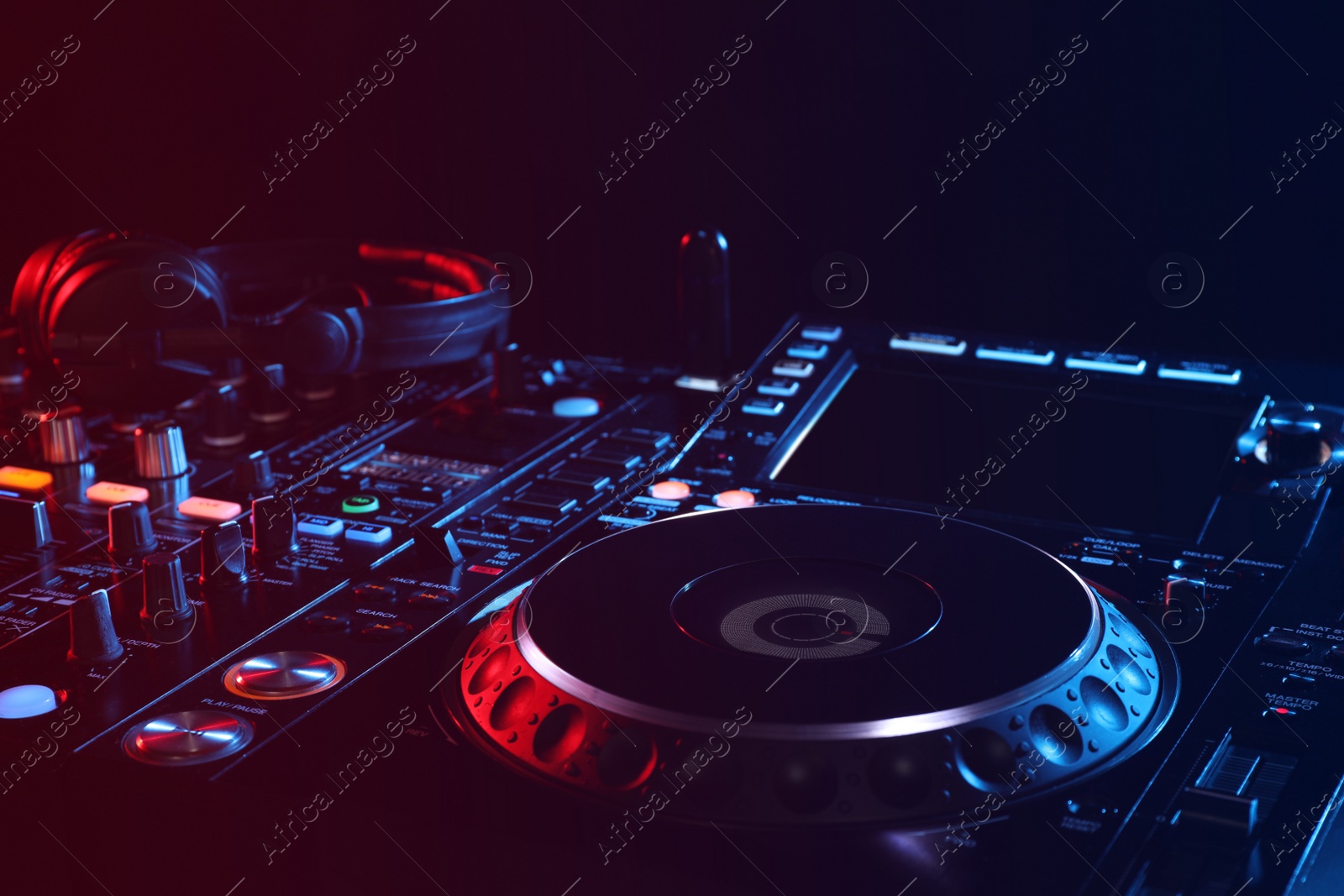 Photo of Closeup view of modern DJ controller with headphones on black background