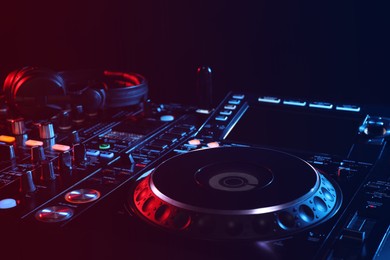 Photo of Closeup view of modern DJ controller with headphones on black background