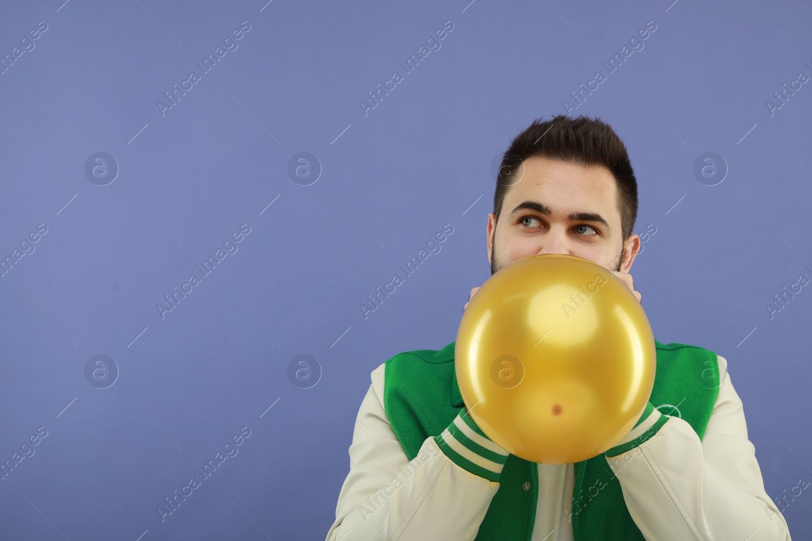Photo of Man inflating bright balloon on violet background, space for text