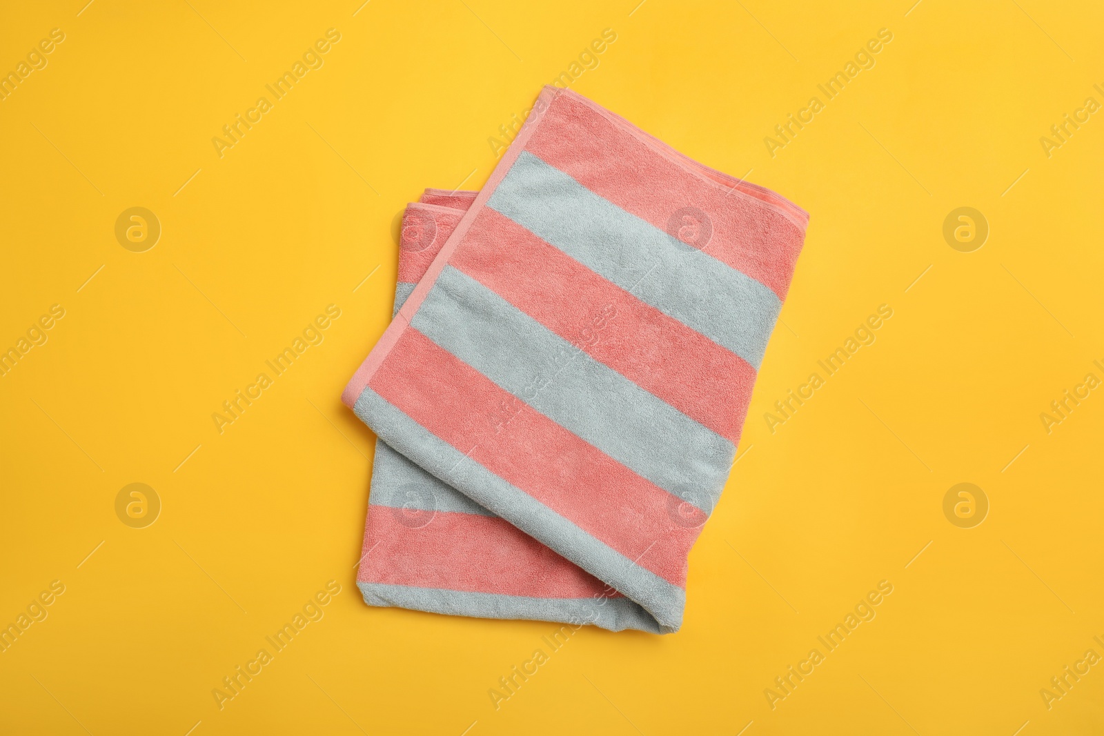 Photo of Folded striped beach towel on yellow background, top view