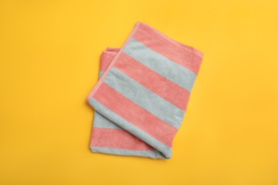 Folded striped beach towel on yellow background, top view