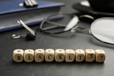 Photo of Wooden cubes with word Blacklist and office stationery on black desk, closeup