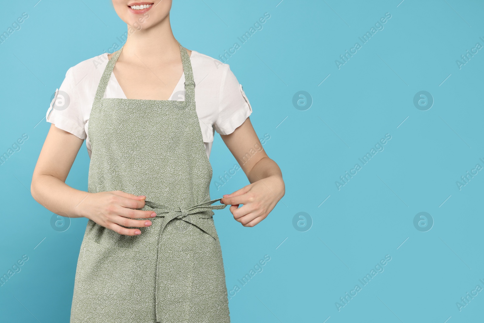 Photo of Woman in clean apron with pattern on light blue background, closeup. Space for text