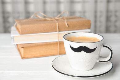 Photo of Cup with paper moustache and books on white wooden table. Happy Father's Day