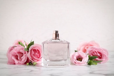 Photo of Bottle of perfume and beautiful flowers on white marble table
