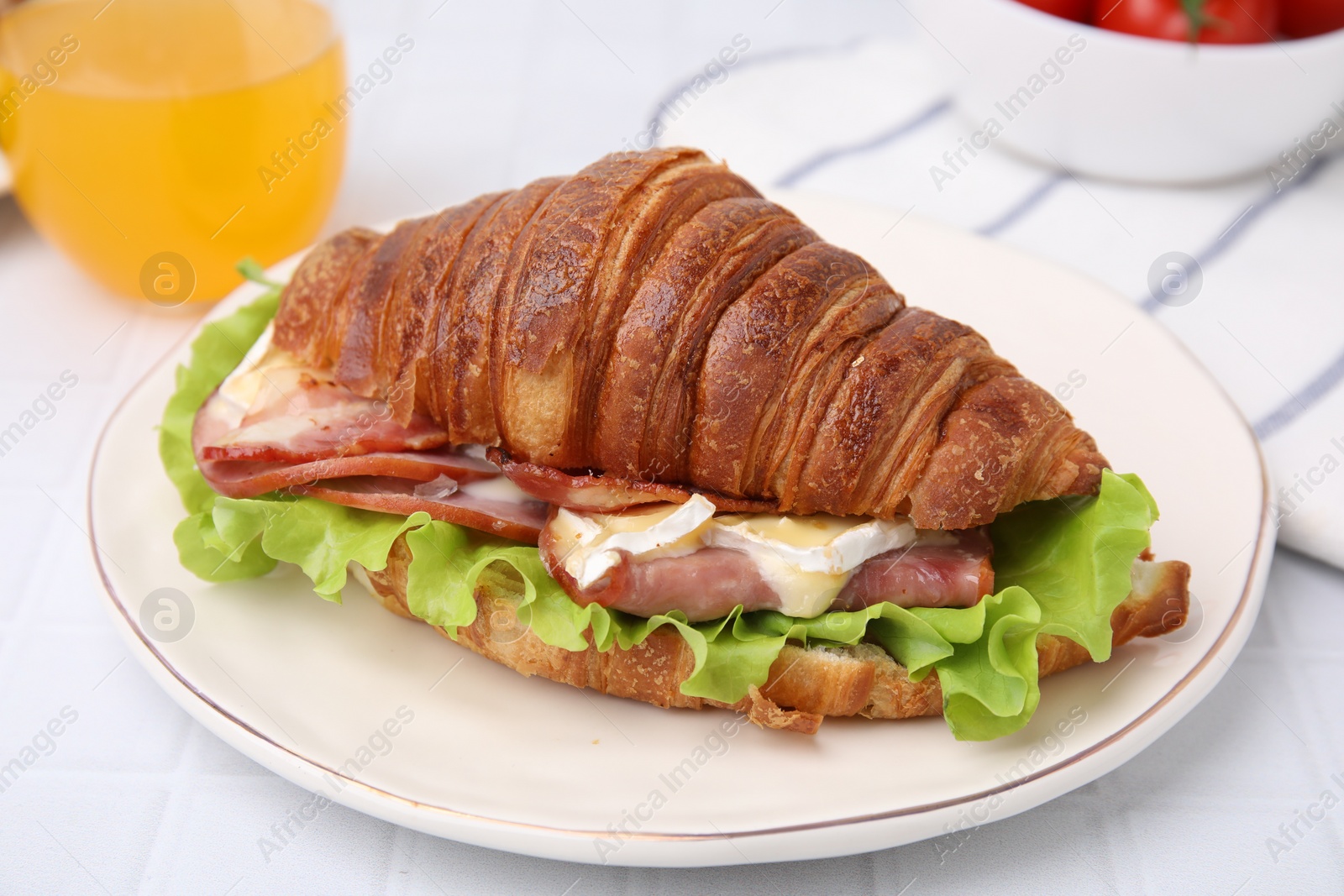 Photo of Tasty croissant with brie cheese, ham and bacon on white table, closeup