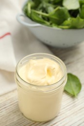 Jar of delicious mayonnaise and fresh spinach on white wooden table