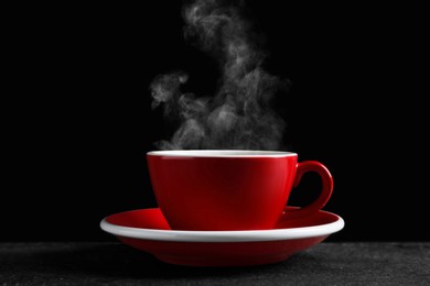 Image of Red cup with hot steaming coffee on dark table against black background