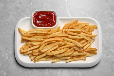 Photo of Plate of tasty french fries served with ketchup on light grey marble table, top view