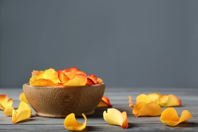 Photo of Bowl with rose petals on wooden table, space for text