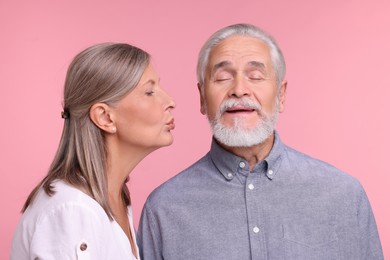 Photo of Senior woman kissing her beloved man on pink background