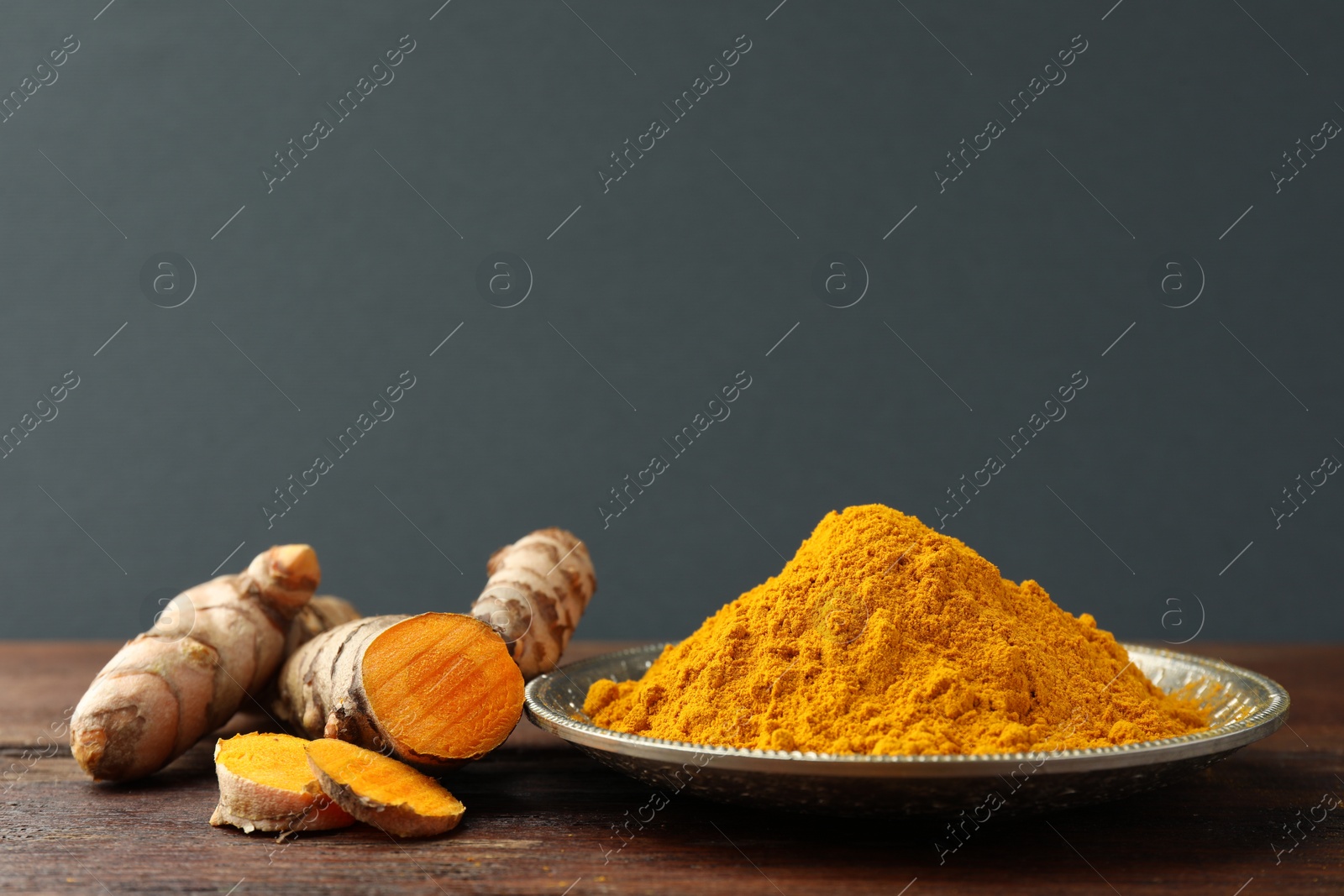 Photo of Plate with aromatic turmeric powder and cut roots on wooden table. Space for text