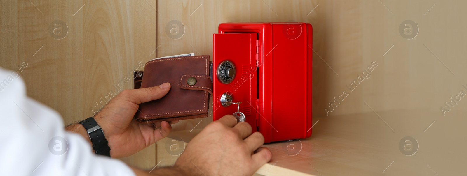 Image of Man putting wallet into small red steel safe, closeup. Banner design