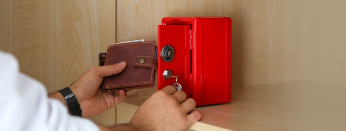 Image of Man putting wallet into small red steel safe, closeup. Banner design