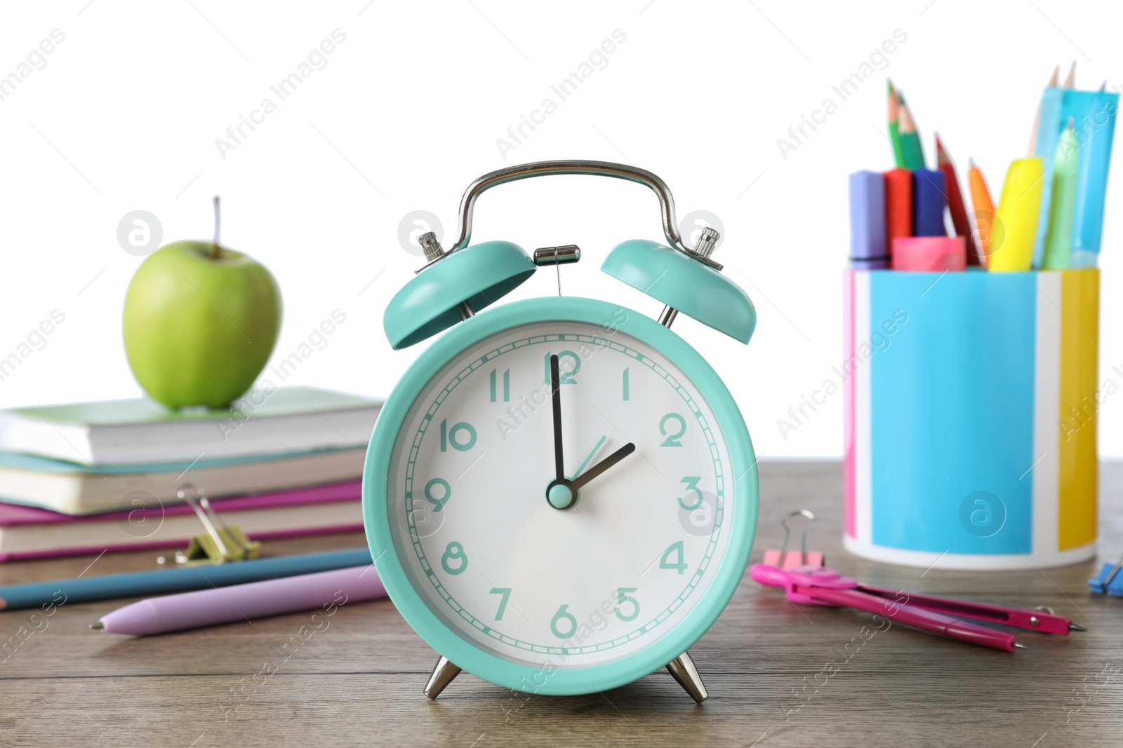 Photo of Turquoise alarm clock and different stationery on wooden table against white background. School time