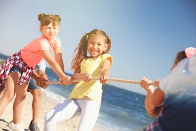 Cute children pulling rope during tug of war game on beach. Summer camp