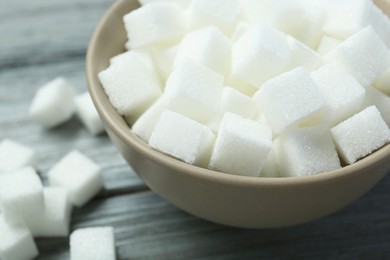 Photo of White sugar cubes in bowl on wooden table, closeup