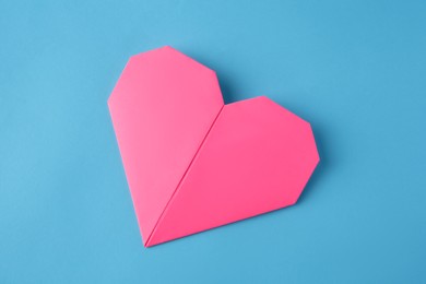 Photo of Origami art. Handmade pink paper heart on light blue background, top view