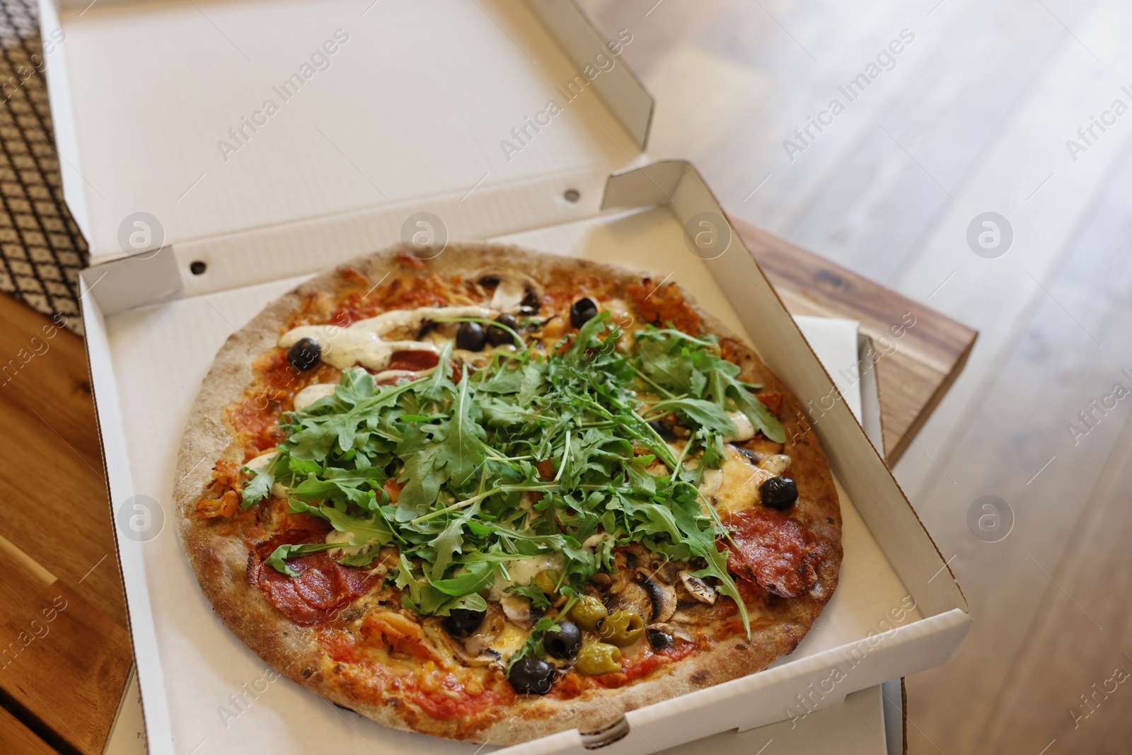 Photo of Delicious pizza with arugula, mushrooms and olives in box on wooden table