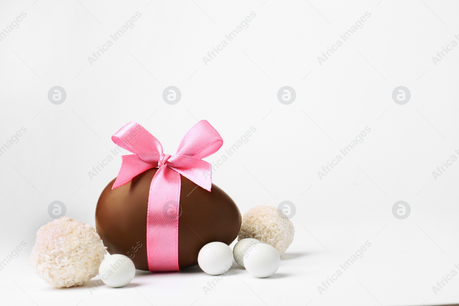 Photo of Sweet chocolate egg with pink bow and different candies on light background, space for text