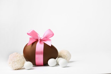 Photo of Sweet chocolate egg with pink bow and different candies on light background, space for text