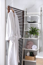 Photo of Beautiful green fern, towels and toiletries on shelving unit in bathroom