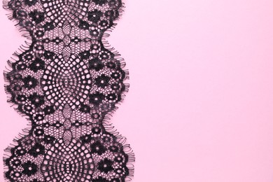 Black lace on pink background, top view. Space for text