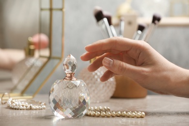 Photo of Woman reaching for crystal bottle of luxurious perfume on dressing table, closeup