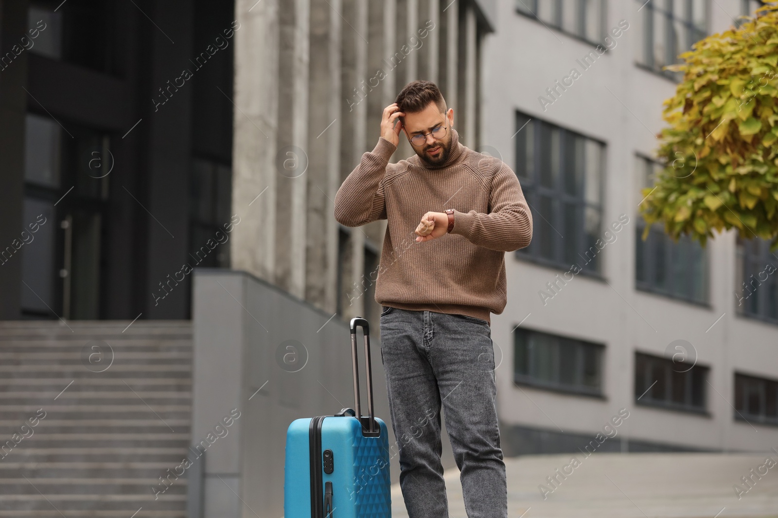 Photo of Being late. Worried man with suitcase looking at watch outdoors, space for text