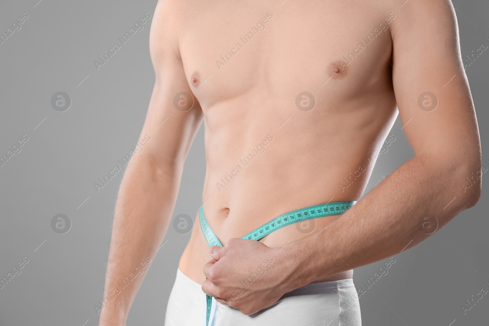 Photo of Young man with measuring tape showing his slim body on grey background