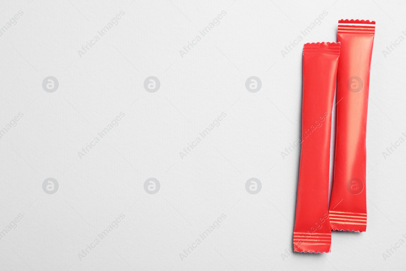 Photo of Red sticks of sugar on light grey background, flat lay. Space for text