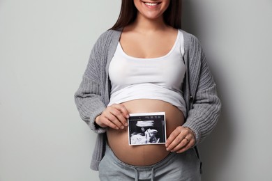Photo of Young pregnant woman with ultrasound picture of baby on grey background, closeup