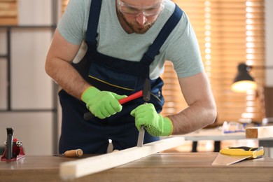 Photo of Carpenter working with hammer and chisel at table indoors