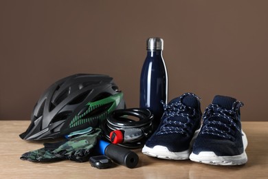 Photo of Different cycling accessories on wooden table against brown background