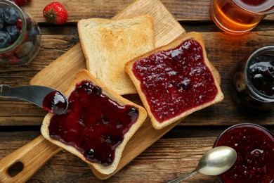 Photo of Delicious toasts served with different jams, tea and berries on wooden table, flat lay