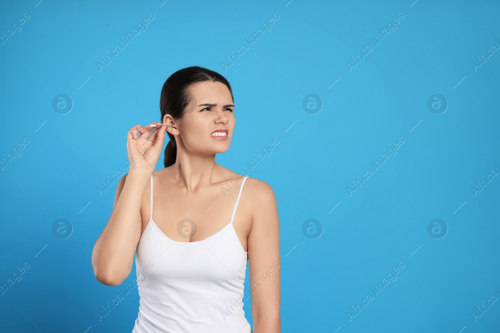 Photo of Young woman cleaning ear with cotton swab on light blue background, space for text