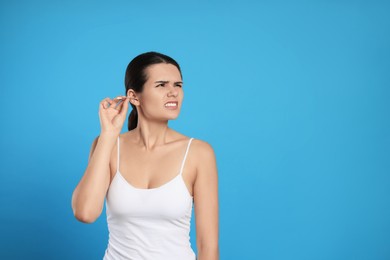 Young woman cleaning ear with cotton swab on light blue background, space for text