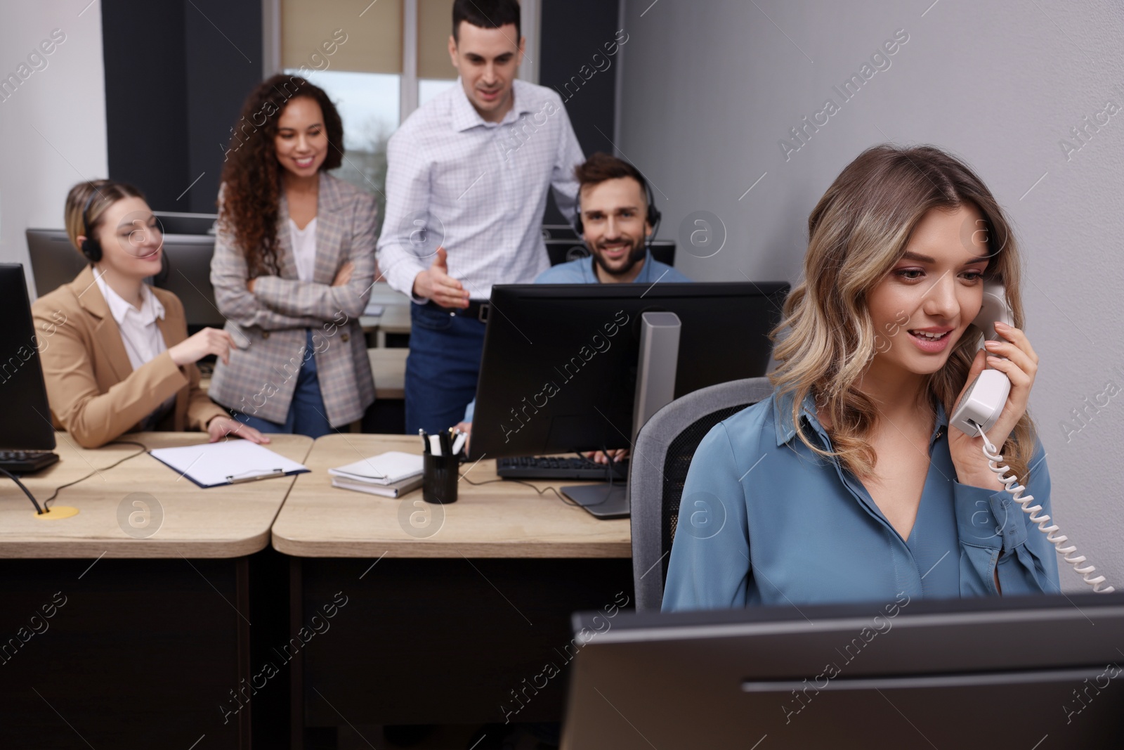 Photo of Young call center operator talking on phone and her colleagues working in modern office