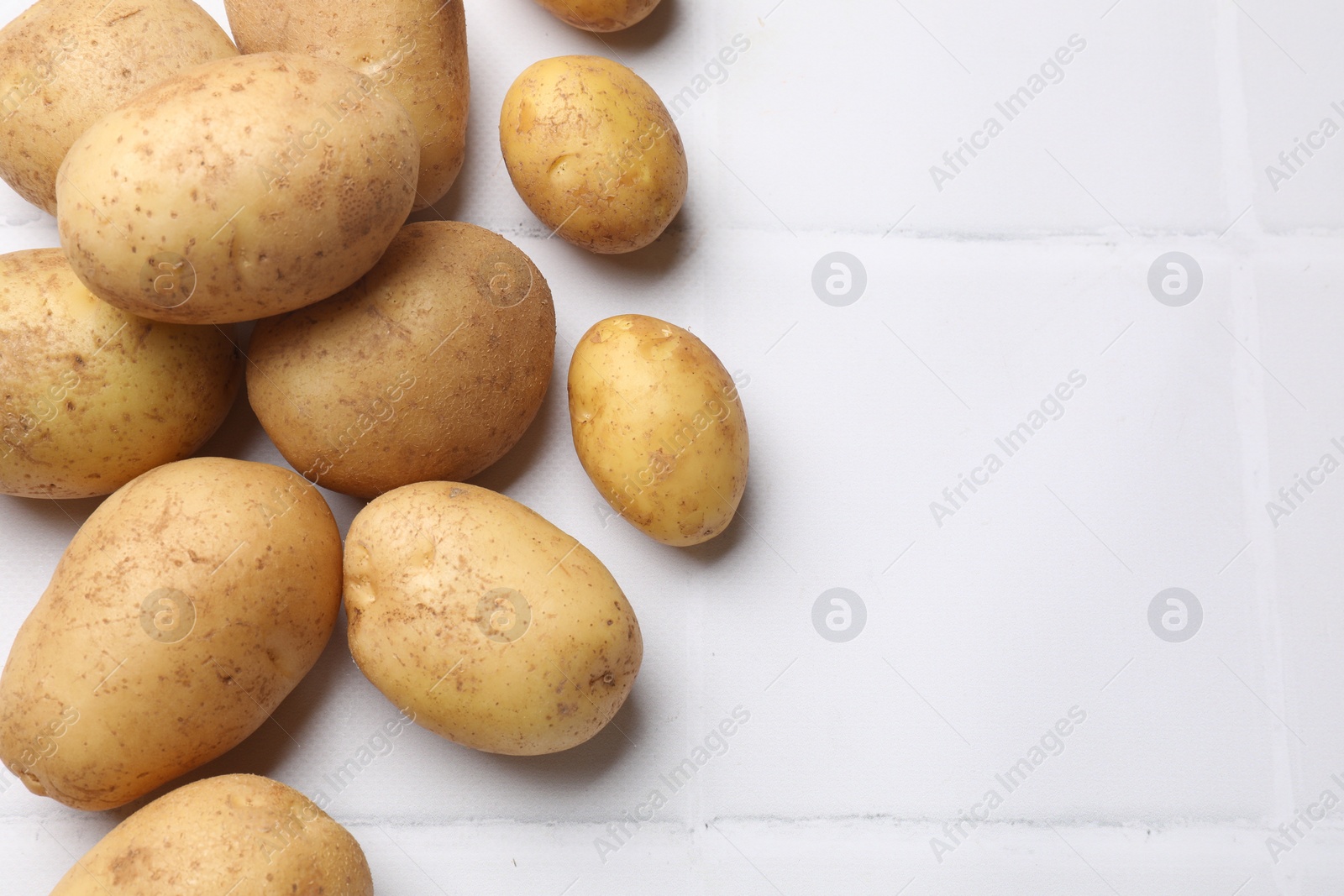 Photo of Raw fresh potatoes on white tiled table, top view. Space for text