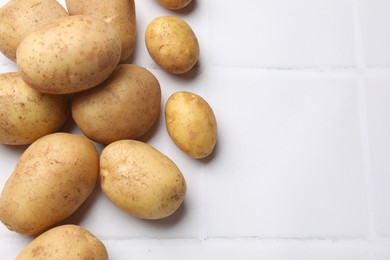 Photo of Raw fresh potatoes on white tiled table, top view. Space for text