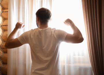 Photo of Man stretching near window indoors. Lazy morning