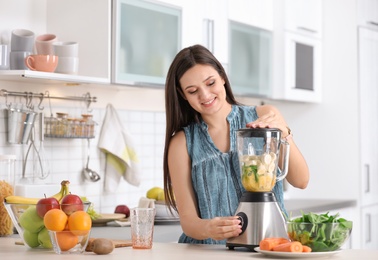 Young woman preparing tasty healthy smoothie at table in kitchen