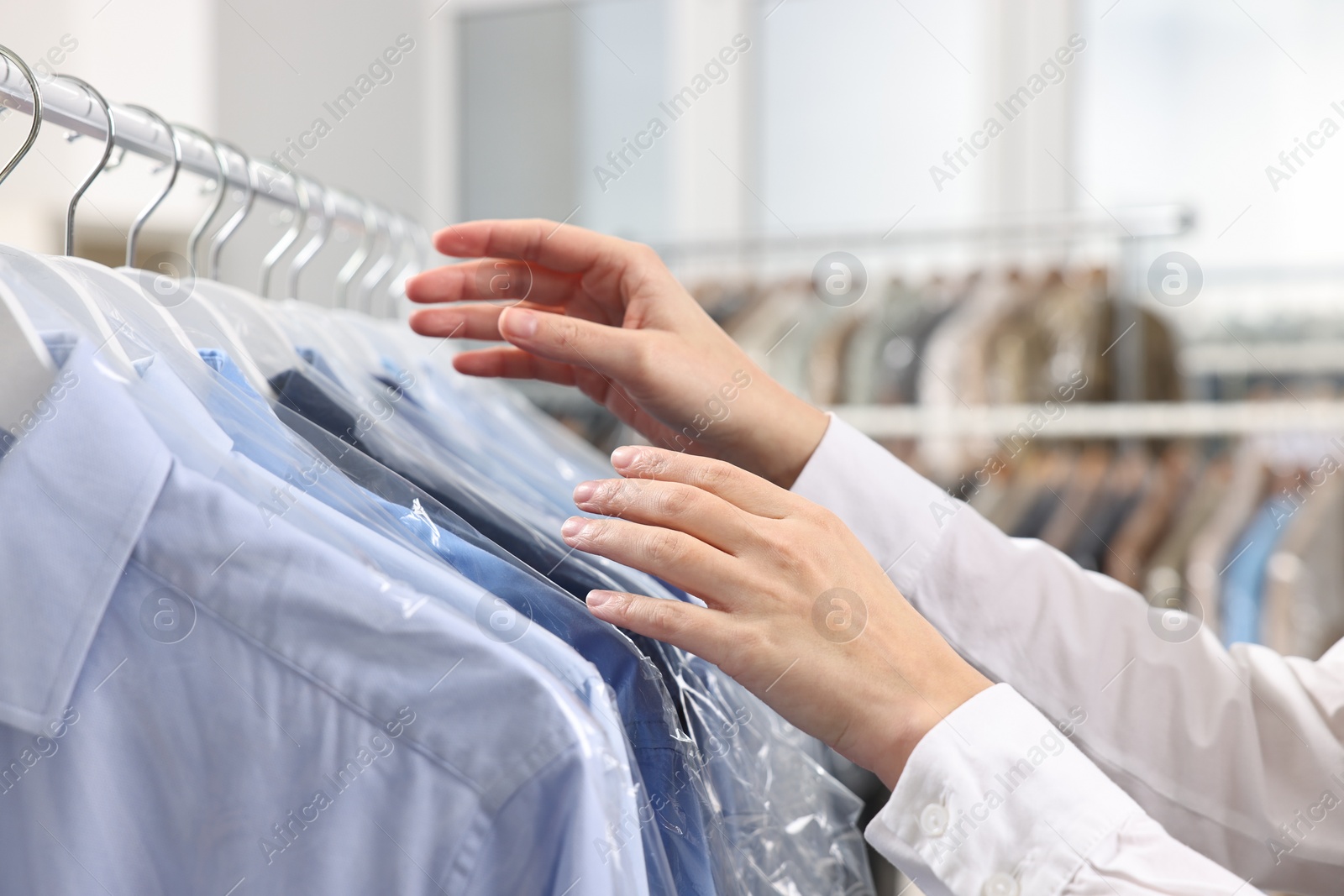 Photo of Dry-cleaning service. Woman taking shirt in plastic bag from rack indoors, closeup