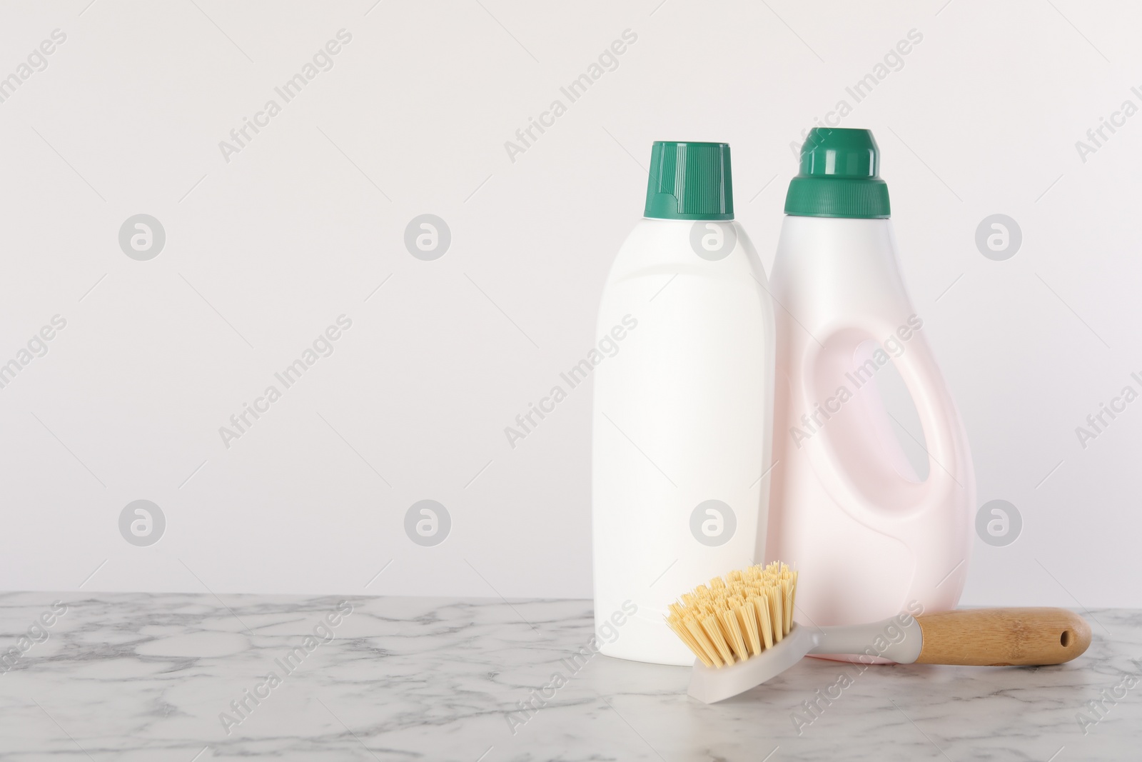 Photo of Bottles of cleaning product and brush on white marble table. Space for text