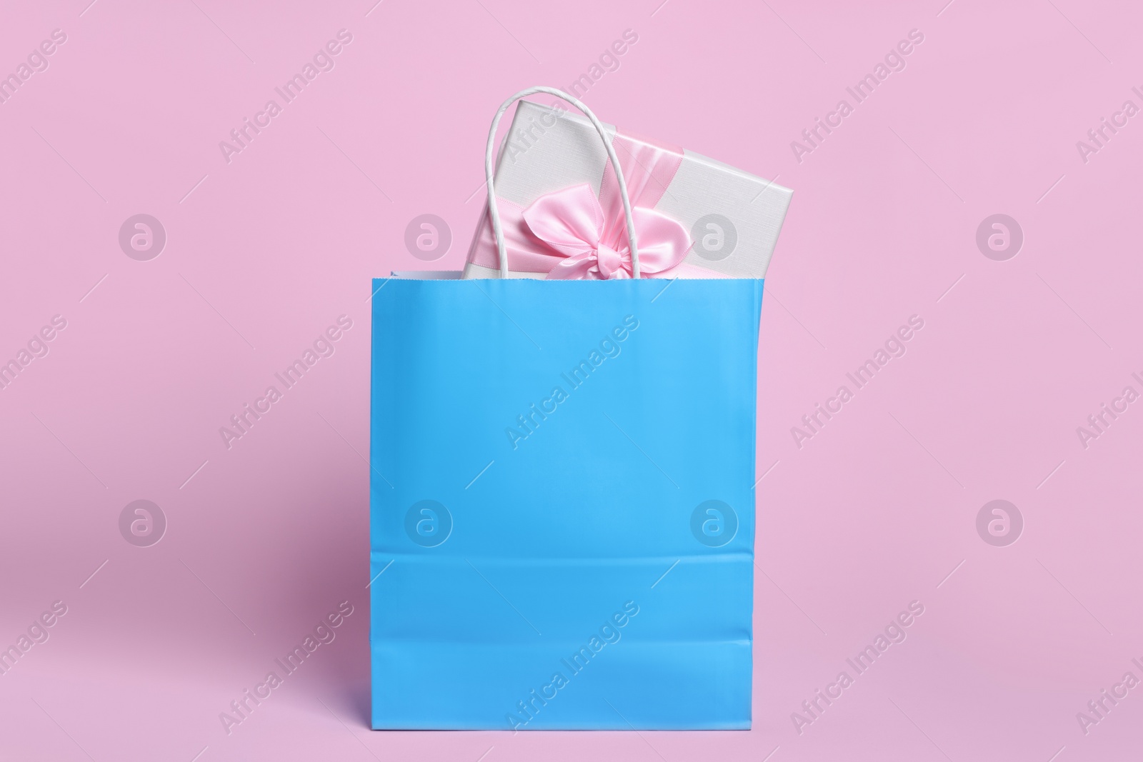 Photo of Light blue paper shopping bag with gift box on pink background